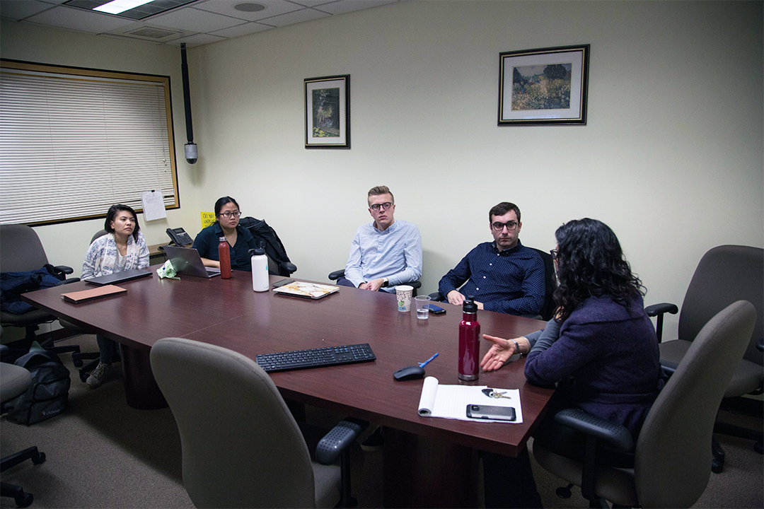 two female students on the left engaging in a discussion with two male students and a professor on the right.