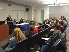 students at table in front of two rows of seated audience