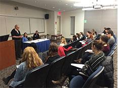 students at table in front of two rows of seated audience