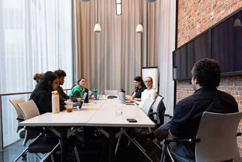 a group of students seated around a table with Professor Dwight Kravitz in a well-lit, spacious room