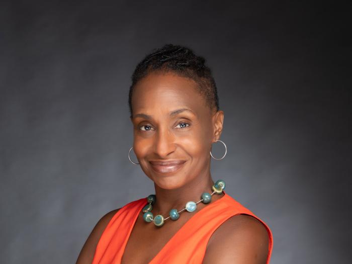 Bowleg standing in an orange outfit with her armed crossed